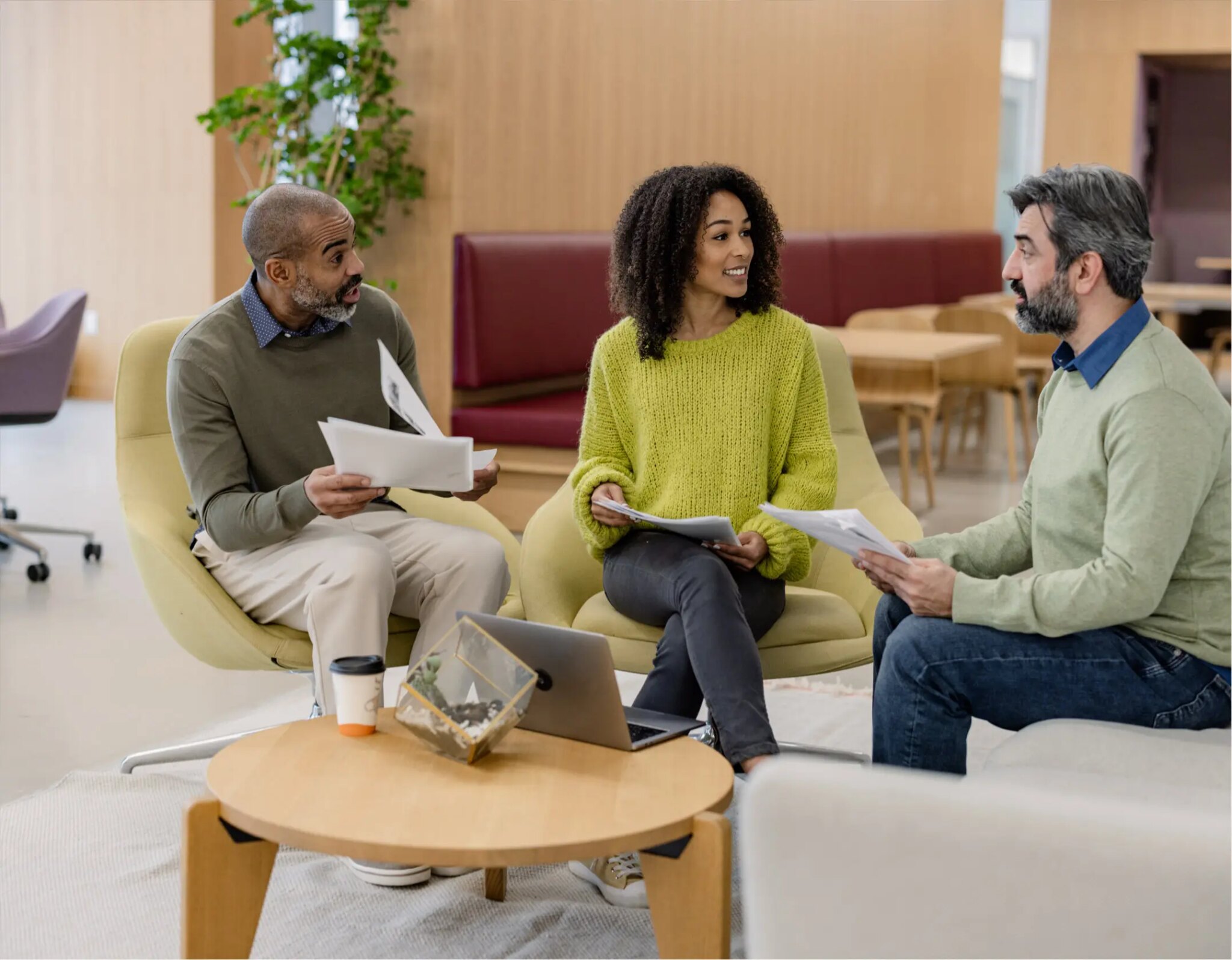 Three professionals reviewing financial documents in modern open-plan office lounge