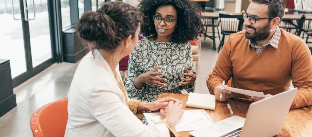 Black female broker in green dress discussing home loan with couple at caf&eacute; table