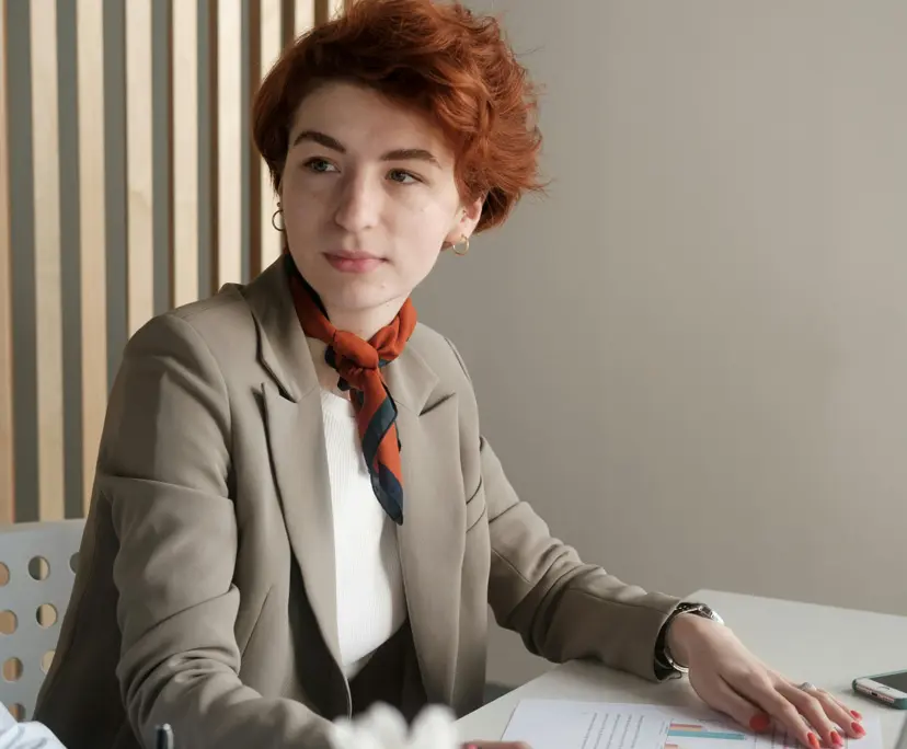 Red-haired financial advisor in tan blazer reviewing charts at desk in modern office