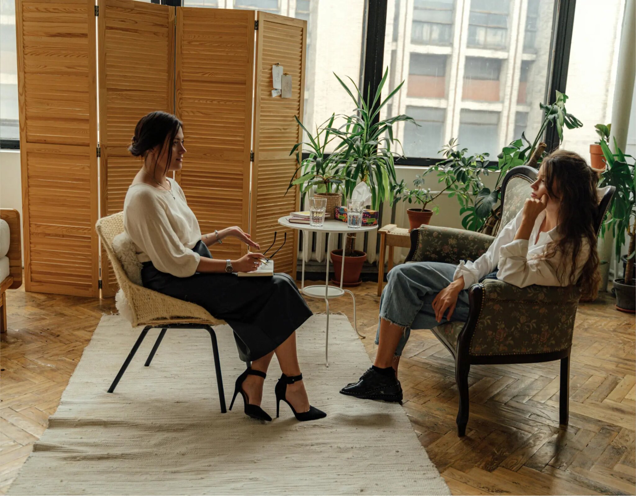 Two women in urban therapy session office seated across from each other by wooden screen